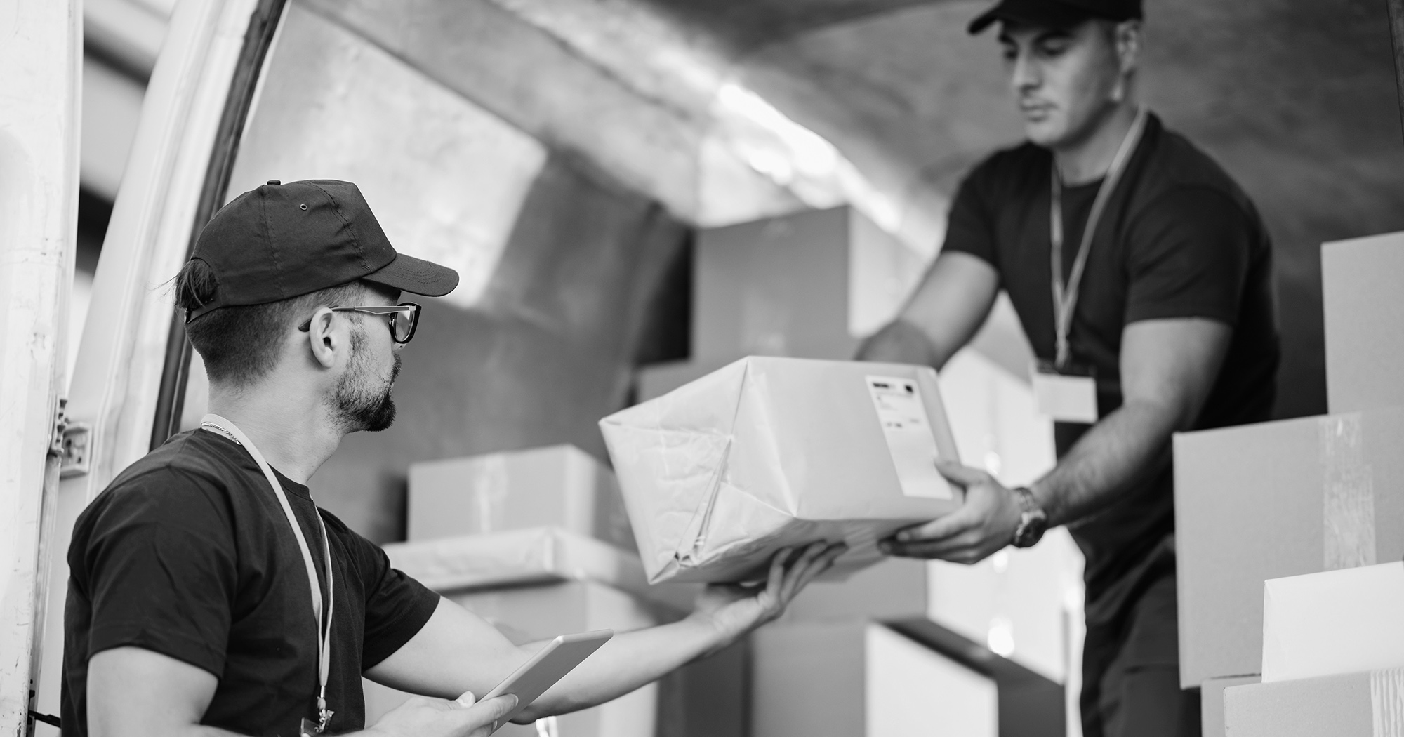 Ecommerce staffing worker hands boxes out of truck to another worker.