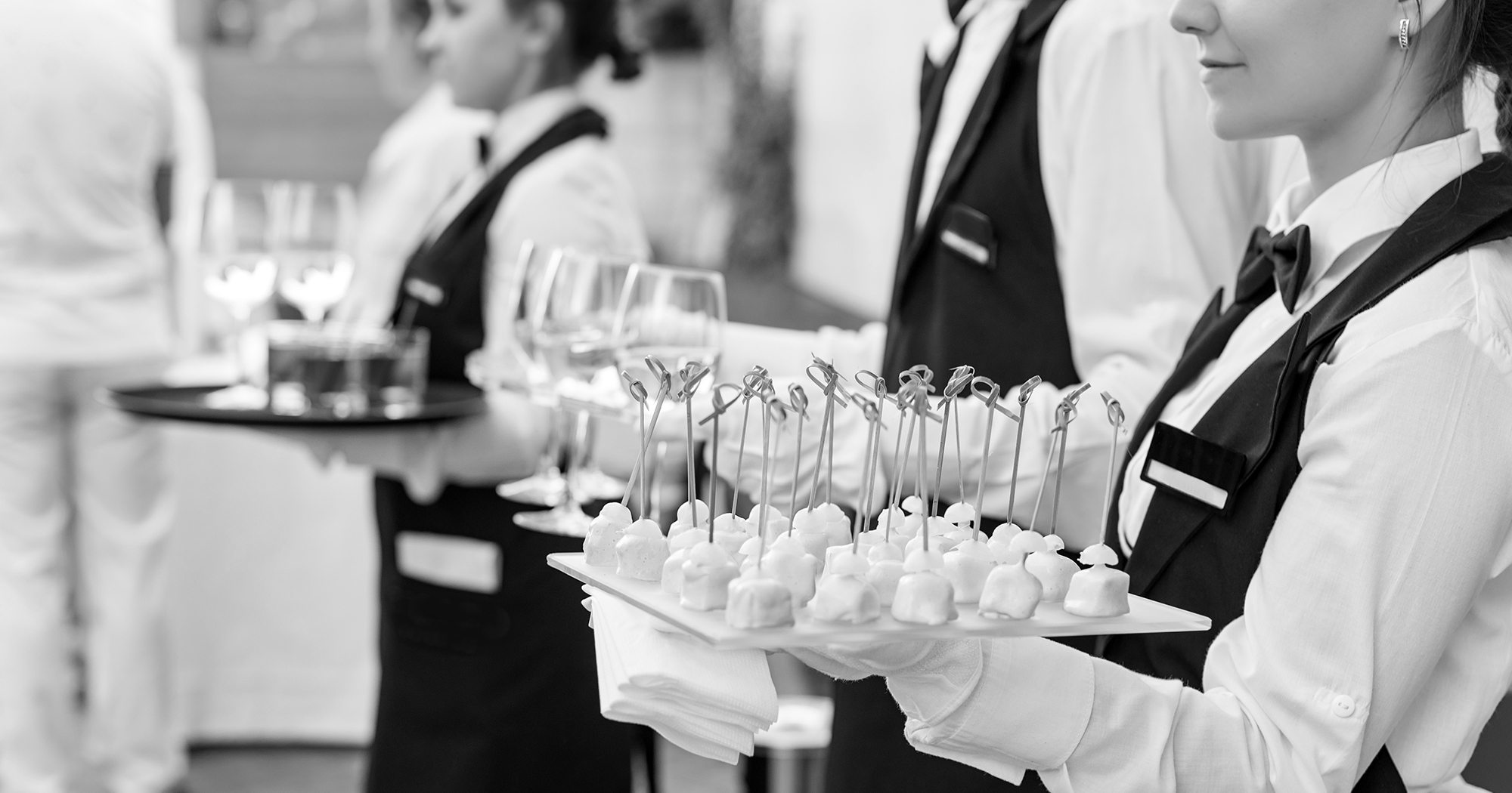 Hospitality catering staff holding trays of appetizers and drinks for guests.
